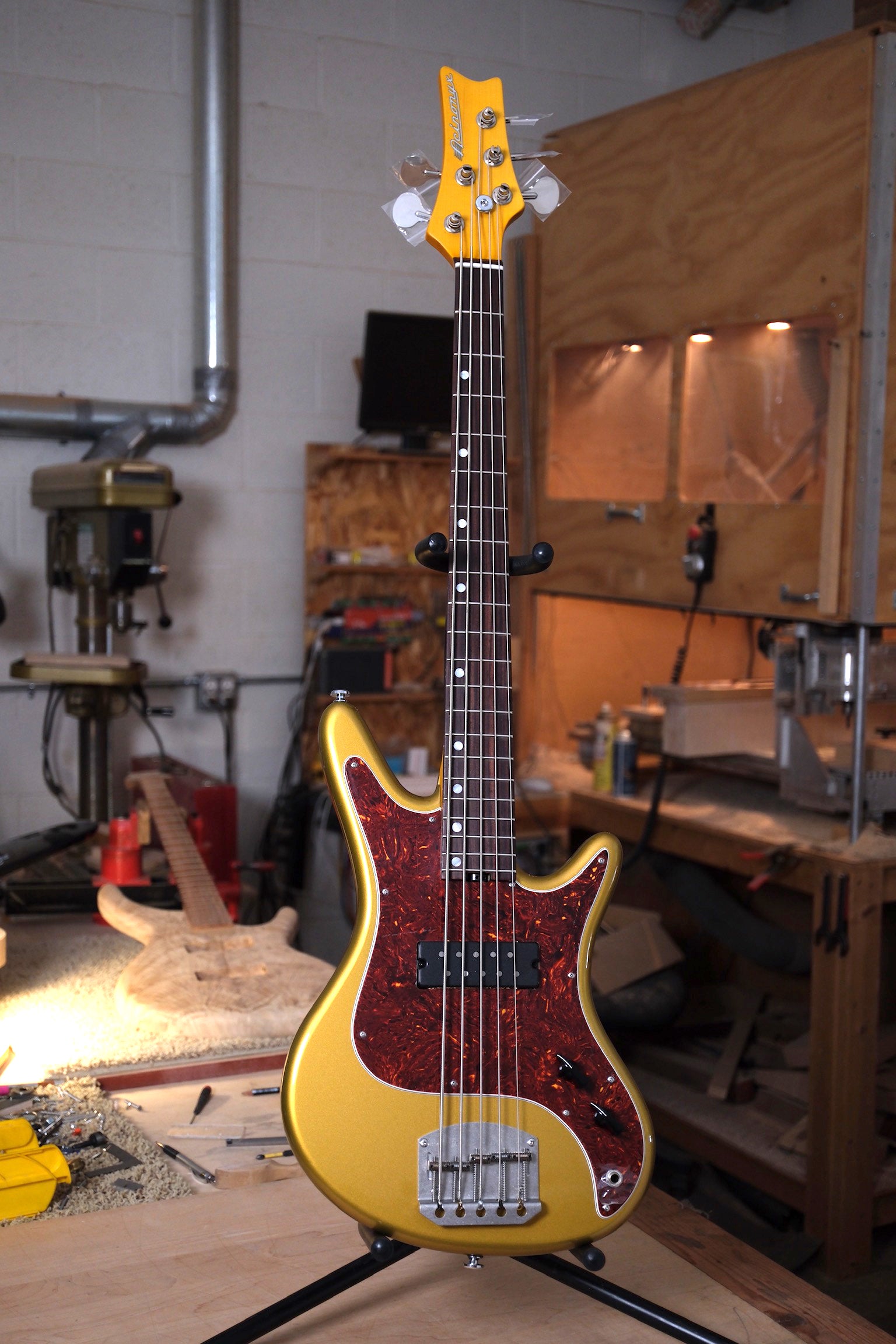 Photo of the Acinonyx V Short Scale Bass Guitar - Aztec Gold showing the full length of the bass in a workshop setting.