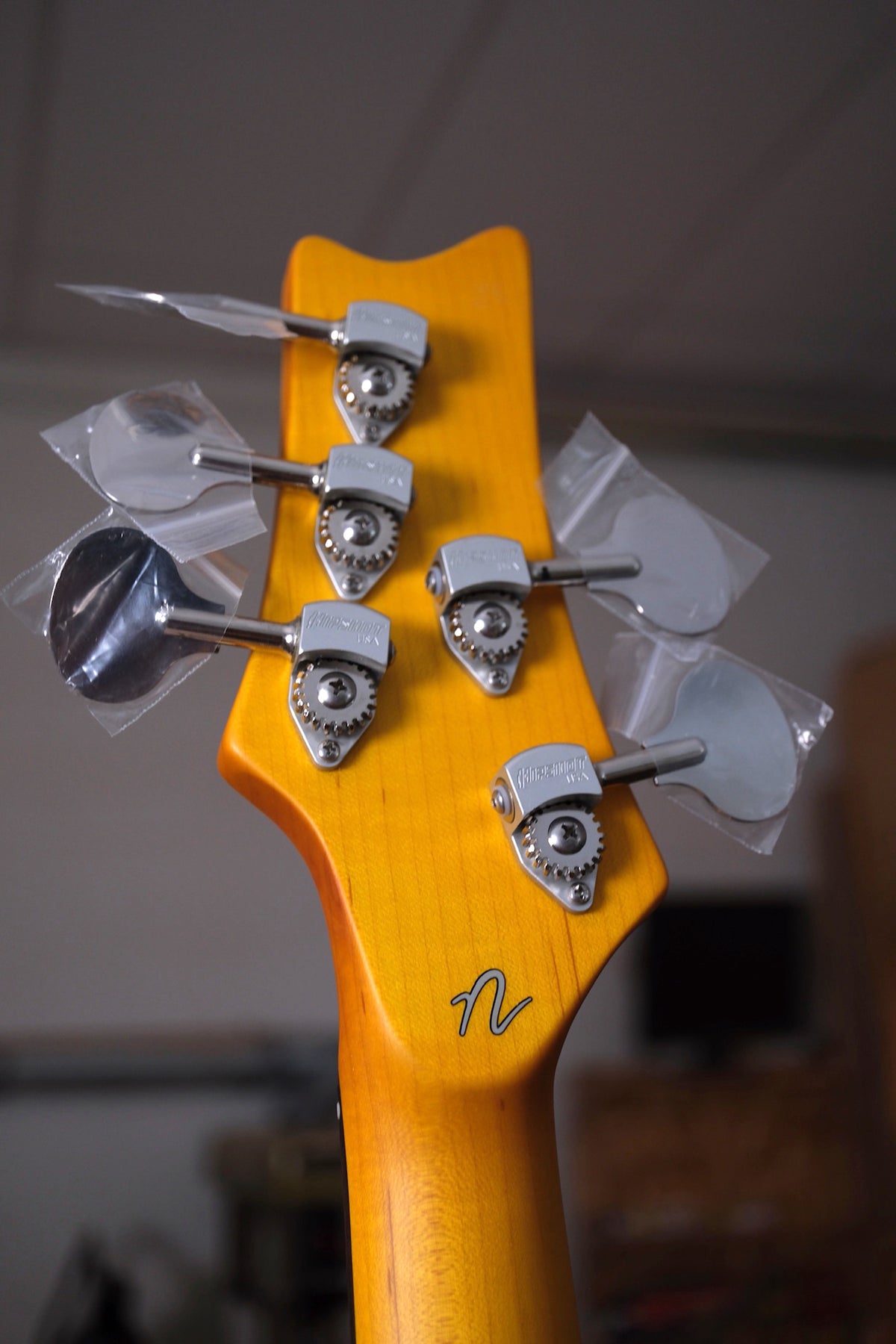 image of the back of the Acinonyx V Short Scale Bass Guitar - Inca Silver sowing the lollipop tuners and the N logo on the volute